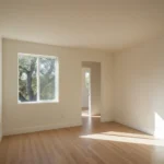 A completed home addition room with white walls, new hardwood floors, and a casement window overlooking a California oak tree.